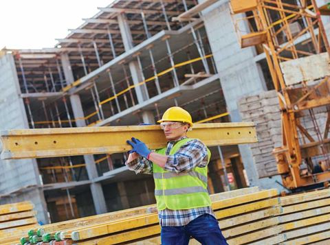 Man on construction site wearing high vis and other PPE carrying steel beam.